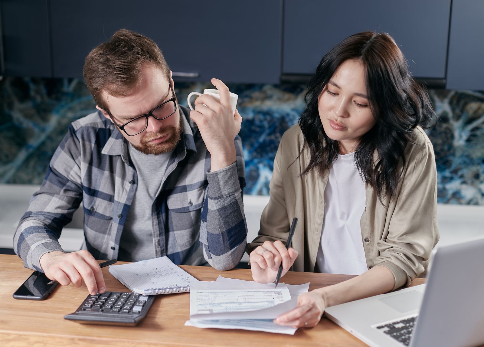 Un couple revoit des factures et un carnet, à la table de la cuisine.