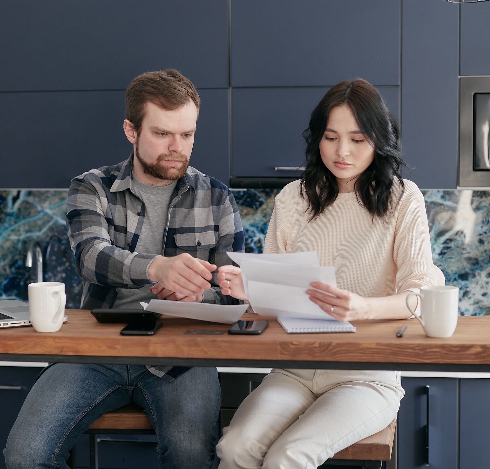 Un couple compare des papiers, assis à la table de la cuisine.